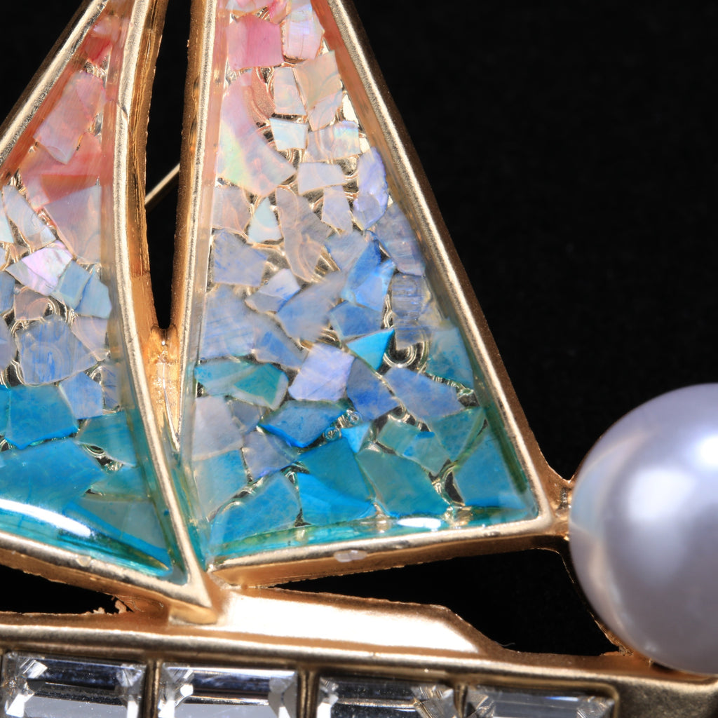 Close up of mother of pearl,nacre shell brooch＆sailboat brooch on black